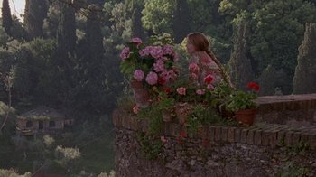 Movie still from “Enchanted April” (1991), directed by Mike Newell – A woman sitting on a wall with flowers in a garden; Wide shot, High angle