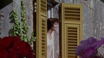 Movie still from “Enchanted April” (1991), directed by Mike Newell – A woman looking out of a window at a building; Medium shot, Low angle