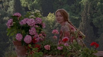 Movie still from “Enchanted April” (1991), directed by Mike Newell – A woman standing next to a flower garden; Medium shot, Over the shoulder angle
