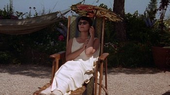 Movie still from “Enchanted April” (1991), directed by Mike Newell – A woman sitting in a chair with an open umbrella; Medium shot, High angle