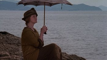 Movie still from “Enchanted April” (1991), directed by Mike Newell – A woman sitting under an umbrella near the ocean; Medium shot, High angle