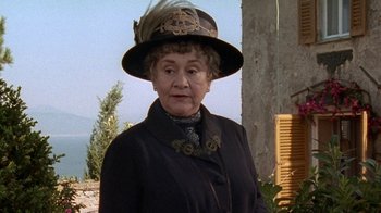 Movie still from “Enchanted April” (1991), directed by Mike Newell – An older woman wearing a hat and a black coat; Close Up shot, Low angle