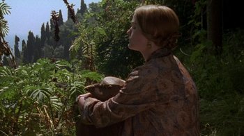 Movie still from “Enchanted April” (1991), directed by Mike Newell – A woman in a floral dress holding a basket in a forest; Medium shot, Over the shoulder angle