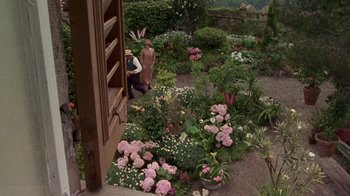 Movie still from “Enchanted April” (1991), directed by Mike Newell – A man standing in a garden with pink and white flowers; Extreme Wide shot, High angle