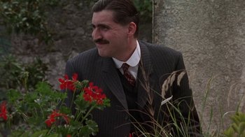 Movie still from “Enchanted April” (1991), directed by Mike Newell – A man in a suit standing next to flowers; Close Up shot, Low angle