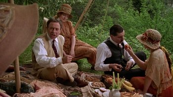 Movie still from “Enchanted April” (1991), directed by Mike Newell – A group of people sitting on a blanket in the grass; Medium shot, High angle