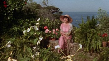 Movie still from “Enchanted April” (1991), directed by Mike Newell – A woman sitting on a rock in a flower garden; Wide shot, High angle