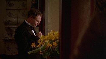 Movie still from “Enchanted April” (1991), directed by Mike Newell – A man standing next to a vase filled with yellow flowers; Medium shot, High angle
