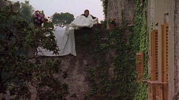 Movie still from “Enchanted April” (1991), directed by Mike Newell – A man laying on top of a wall covered in a blanket; Wide shot, Low angle