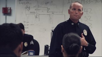 Movie still from “End of Watch” (2012), directed by David Ayer – A man in a police uniform standing in front of a group of people; Medium shot, Over the shoulder angle