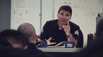Movie still from “End of Watch” (2012), directed by David Ayer – A police officer talking to another officer in a room; Medium shot, Over the shoulder angle