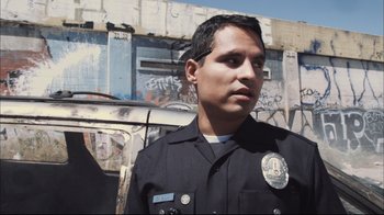 Movie still from “End of Watch” (2012), directed by David Ayer – A man in a police uniform standing in front of a building; Close Up shot, Low angle