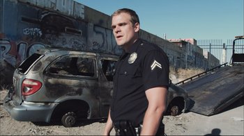 Movie still from “End of Watch” (2012), directed by David Ayer – A police officer standing in front of a burned out car; Medium shot, Low angle
