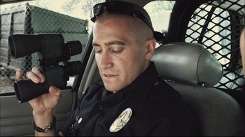 Movie still from “End of Watch” (2012), directed by David Ayer – A police officer sitting in the back of a patrol car while holding a video camera; Close Up shot, Low angle