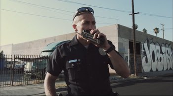 Movie still from “End of Watch” (2012), directed by David Ayer – A police officer talking on a walkie talkie; Medium shot, Low angle