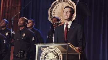 Movie still from “End of Watch” (2012), directed by David Ayer – A man standing at a podium in front of a microphone; Medium shot, Low angle
