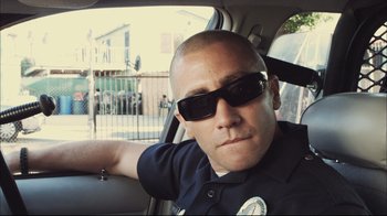 Movie still from “End of Watch” (2012), directed by David Ayer – A police officer sitting in the back of a car wearing sunglasses; Close Up shot, Over the shoulder angle