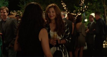 Movie still from “Enough Said” (2013), directed by Nicole Holofcener – A woman holding a glass of champagne talking to another woman; Medium shot, Over the shoulder angle