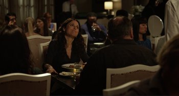 Movie still from “Enough Said” (2013), directed by Nicole Holofcener – A woman sitting at a table holding a tray of food; Medium shot, Over the shoulder angle