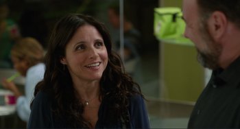 Movie still from “Enough Said” (2013), directed by Nicole Holofcener – A woman with long dark curly hair smiling at the camera; Close Up shot, Over the shoulder angle