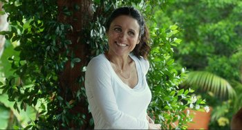 Movie still from “Enough Said” (2013), directed by Nicole Holofcener – A woman standing next to a tree smiling for the camera; Medium shot, Over the shoulder angle