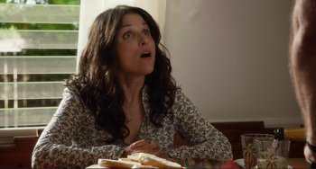 Movie still from “Enough Said” (2013), directed by Nicole Holofcener – A woman sitting at a table with a sandwich in front of her mouth; Close Up shot, Low angle