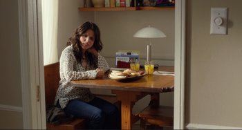 Movie still from “Enough Said” (2013), directed by Nicole Holofcener – A woman sitting at a table with a plate of food; Medium shot, Over the shoulder angle