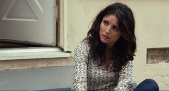 Movie still from “Enough Said” (2013), directed by Nicole Holofcener – A woman sitting on the ground looking at the camera; Close Up shot, High angle