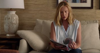 Movie still from “Enough Said” (2013), directed by Nicole Holofcener – A woman sitting on a couch looking at a magazine; Medium shot, Over the shoulder angle