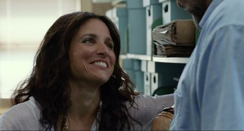 Movie still from “Enough Said” (2013), directed by Nicole Holofcener – A woman smiling at the camera in a room filled with boxes; Close Up shot, Low angle