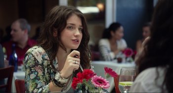 Movie still from “Enough Said” (2013), directed by Nicole Holofcener – A beautiful young lady sitting at a table with flowers; Close Up shot, Over the shoulder angle