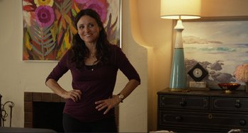 Movie still from “Enough Said” (2013), directed by Nicole Holofcener – A woman standing in front of a lamp in a room; Medium shot, Over the shoulder angle