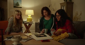 Movie still from “Enough Said” (2013), directed by Nicole Holofcener – Three women are looking at an old photo on a table; Medium shot, Over the shoulder angle