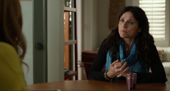 Movie still from “Enough Said” (2013), directed by Nicole Holofcener – A woman sitting at a wooden table in front of a window; Close Up shot, Over the shoulder angle