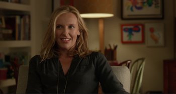 Movie still from “Enough Said” (2013), directed by Nicole Holofcener – A woman sitting in a chair smiling for the camera; Close Up shot, Over the shoulder angle