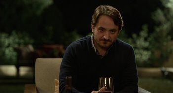 Movie still from “Enough Said” (2013), directed by Nicole Holofcener – A man sitting in front of a glass of wine; Close Up shot, Over the shoulder angle