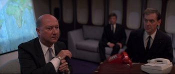 Movie still from “Escape from New York” (1981), directed by John Carpenter – Two men in suits sitting at a table; Medium shot, Low angle