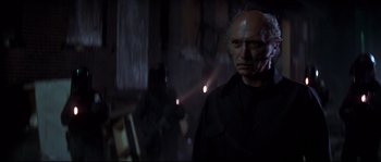 Movie still from “Escape from New York” (1981), directed by John Carpenter – An older man in a black shirt is in a dark room; Close Up shot, Low angle