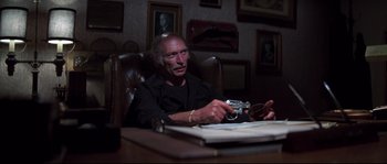 Movie still from “Escape from New York” (1981), directed by John Carpenter – An older man sitting at a desk with a camera; Medium shot, High angle