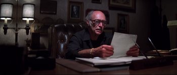 Movie still from “Escape from New York” (1981), directed by John Carpenter – An older man sitting at a table looking at papers; Medium shot, Low angle