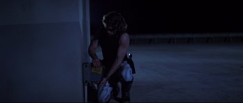 Movie still from “Escape from New York” (1981), directed by John Carpenter – A man in a black shirt is holding a book; Medium shot, Low angle