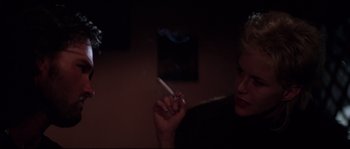 Movie still from “Escape from New York” (1981), directed by John Carpenter – A woman is holding a cigarette in her hand; Close Up shot, Over the shoulder angle