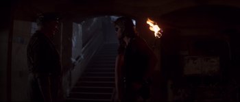 Movie still from “Escape from New York” (1981), directed by John Carpenter – A woman walking up a flight of stairs with torches; Medium shot, Over the shoulder angle
