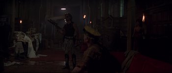 Movie still from “Escape from New York” (1981), directed by John Carpenter – A couple of people that are in a room; Wide shot, Over the shoulder angle