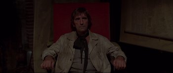 Movie still from “Escape from New York” (1981), directed by John Carpenter – A man sitting in a chair wearing a jacket and tie; Medium shot, Low angle