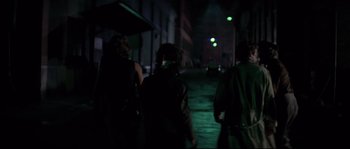 Movie still from “Escape from New York” (1981), directed by John Carpenter – A group of people walking down a street at night; Medium shot, Over the shoulder angle
