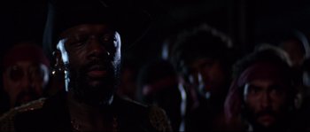 Movie still from “Escape from New York” (1981), directed by John Carpenter – A man with a beard and a hat is in a dark room; Close Up shot, Low angle