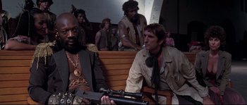 Movie still from “Escape from New York” (1981), directed by John Carpenter – A group of men sitting next to each other on a bench; Medium shot, Low angle