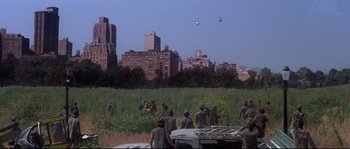 Movie still from “Escape from New York” (1981), directed by John Carpenter – A group of people standing in a field with buildings in the background; Extreme Wide shot, High angle