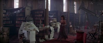Movie still from “Escape from New York” (1981), directed by John Carpenter – A woman walking through a library holding a camera; Wide shot, High angle
